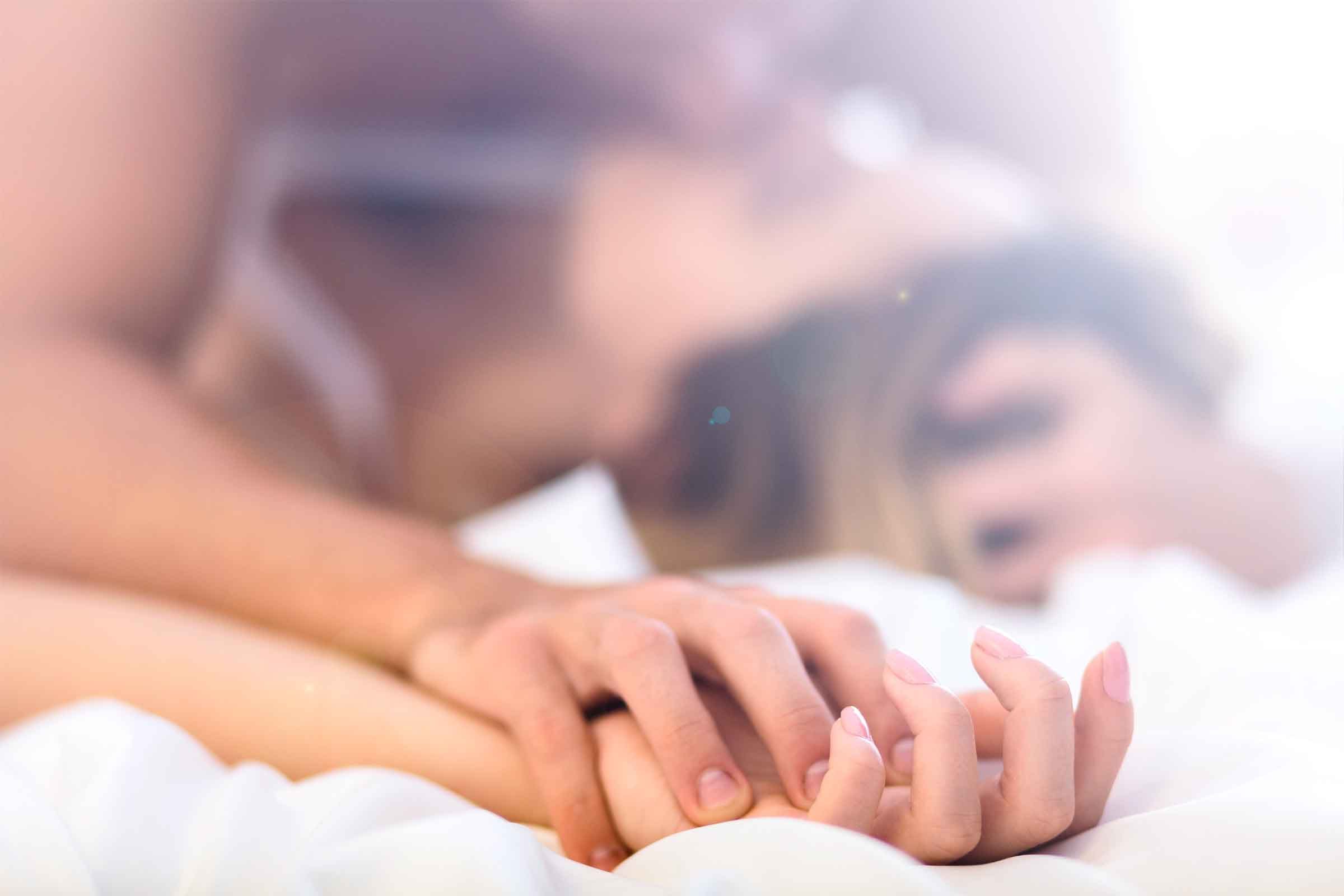 Close up hand of female and male hands clasped together in bed, kissing in background|Close up hand of female pulling white sheets in ecstasy , feeling and emotion concept