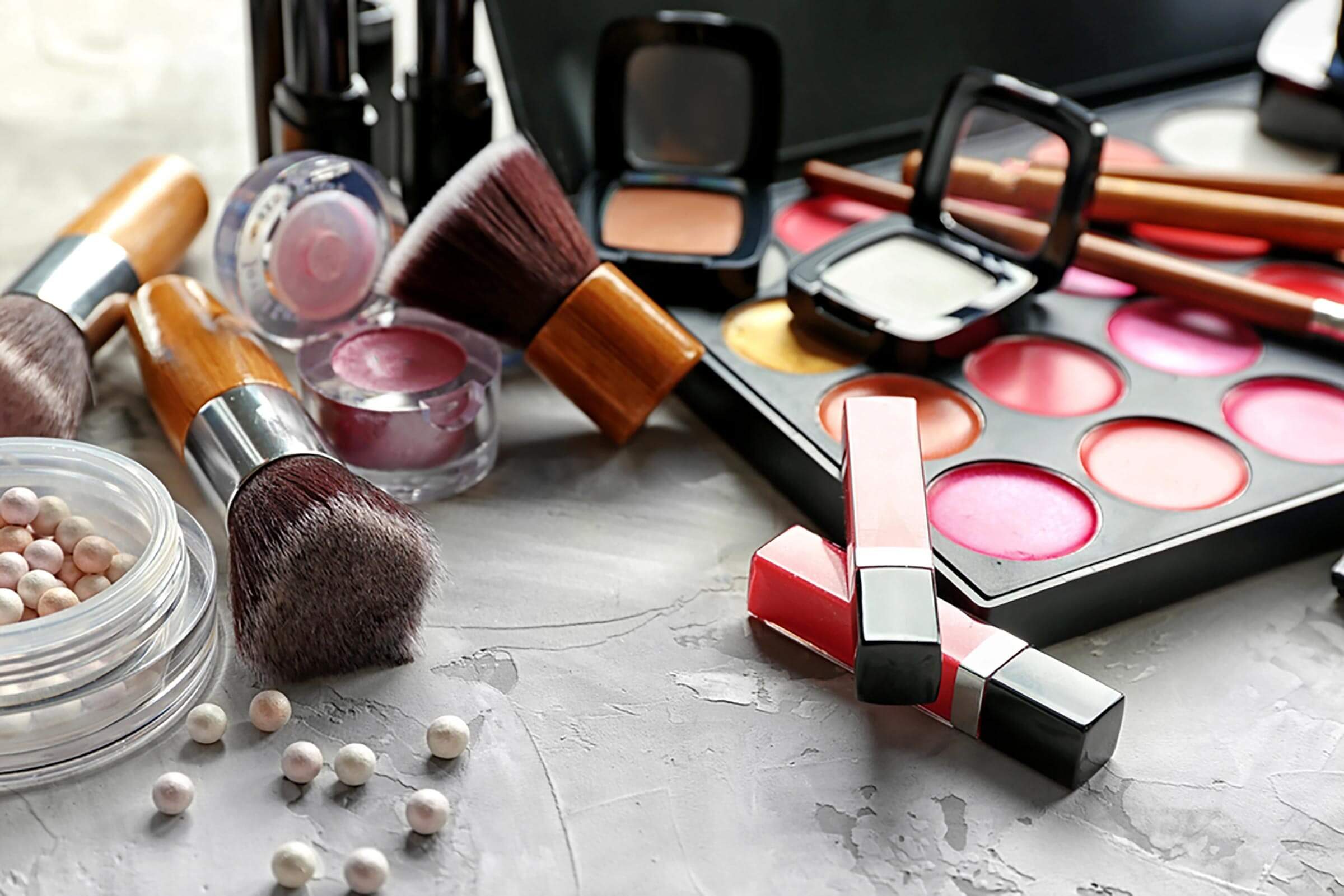 A makeup set, including blushes, lip glosses, and brushes, on a marble counter.