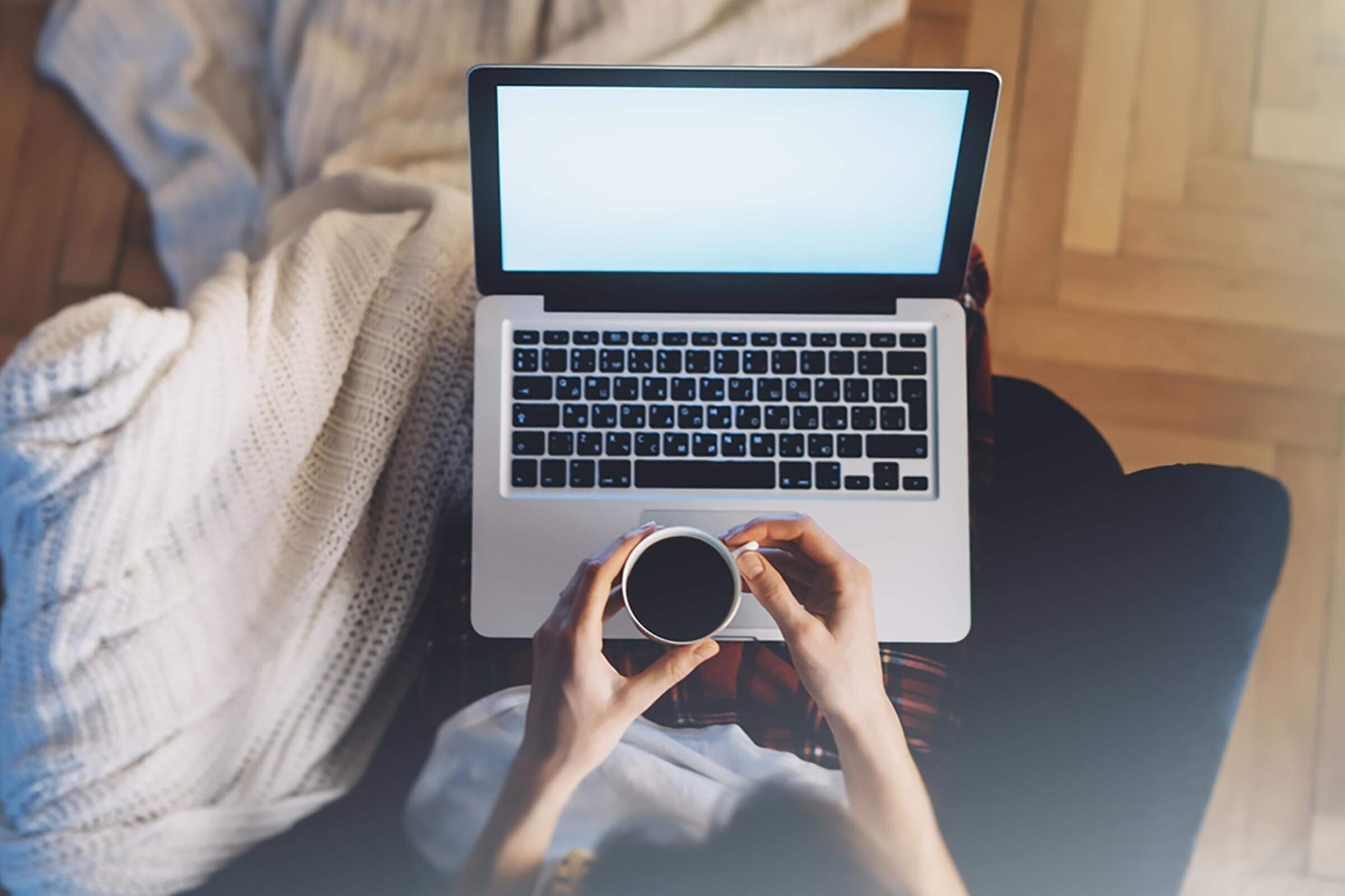 A person with their laptop computer in their lap while also holding a cup of coffee.
