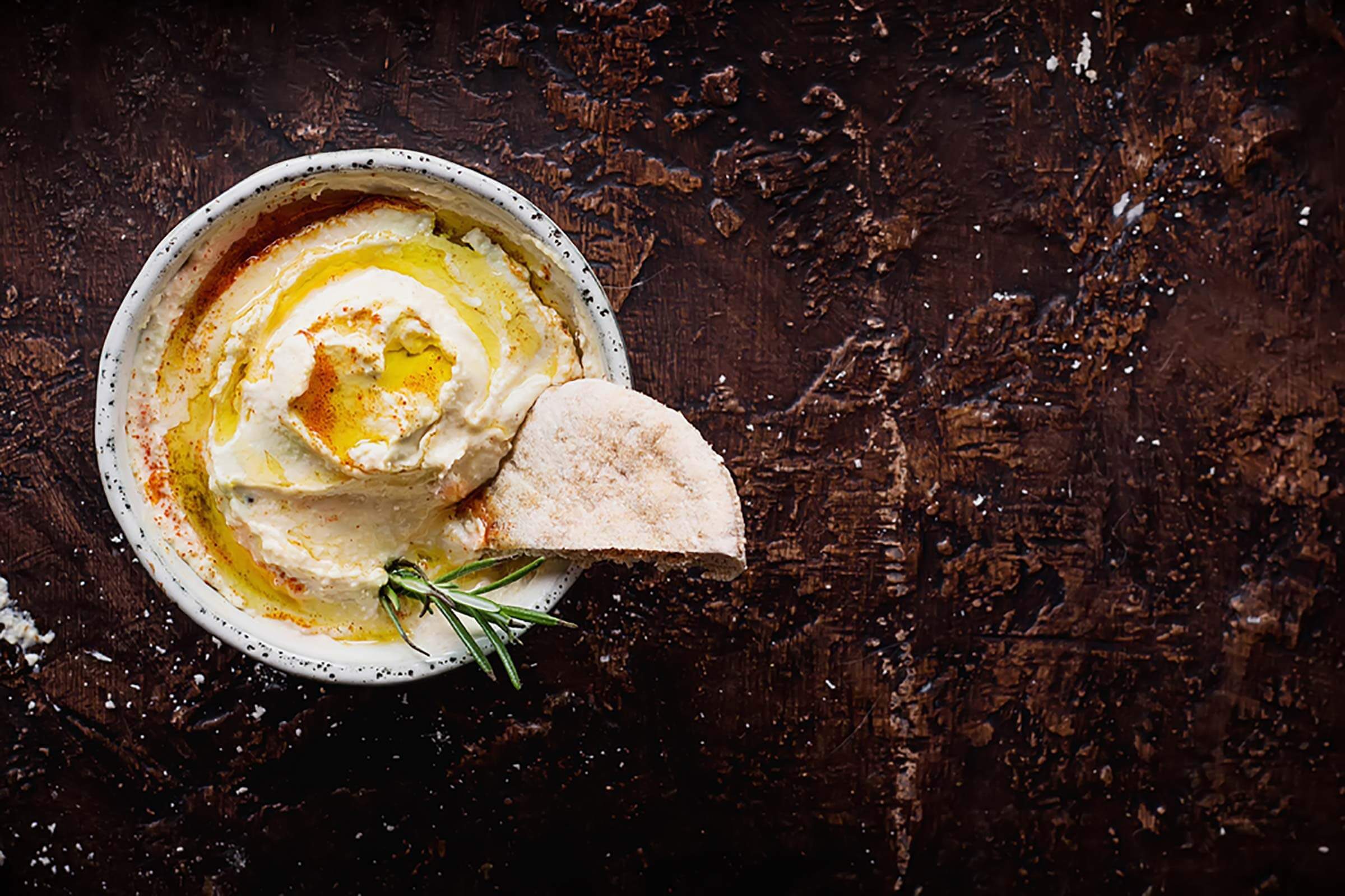 Hummus in a bowl with rosemary and pita