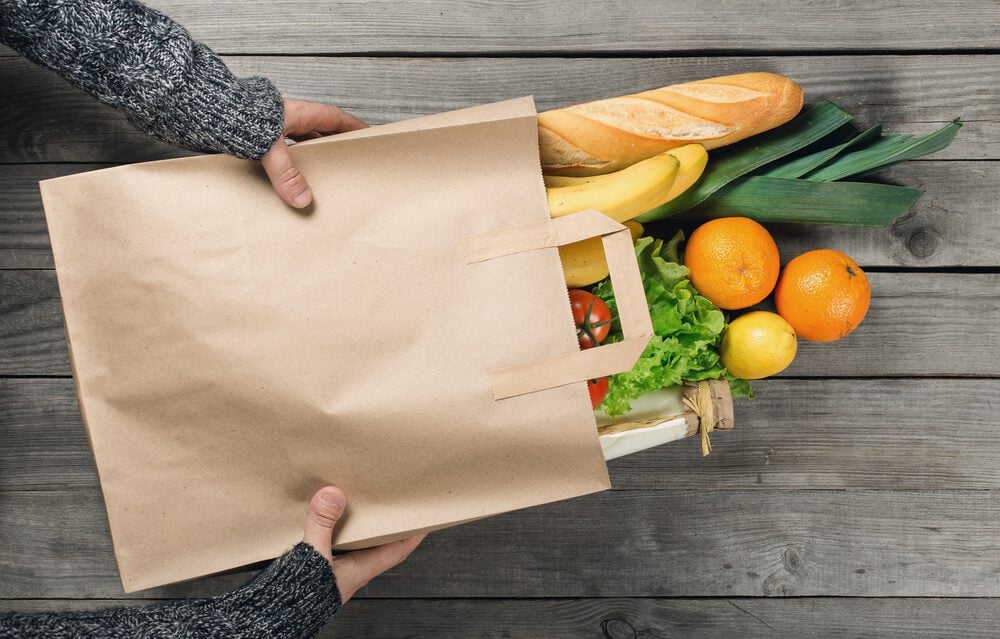 Man's hands holding paper bag of groceries, top view