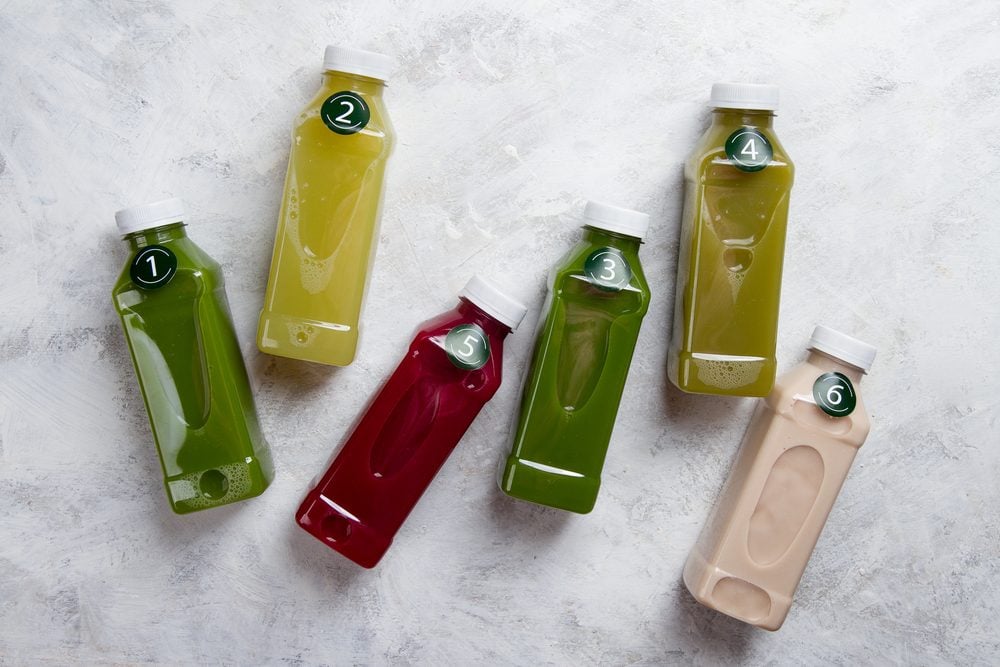 Healthy eating, drinks, diet and detox concept - close up of five plastic bottles with different fruit or vegetable juices for detox plan