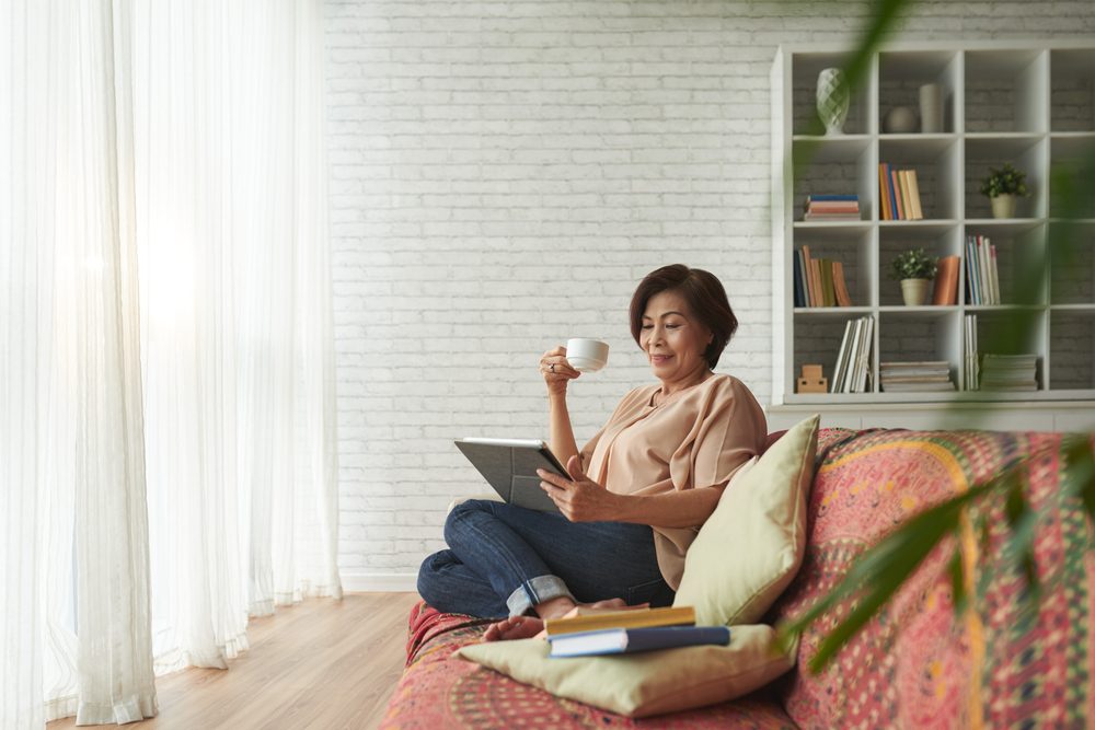 Mujer mayor vietnamita bebiendo té y leyendo un libro en una tableta