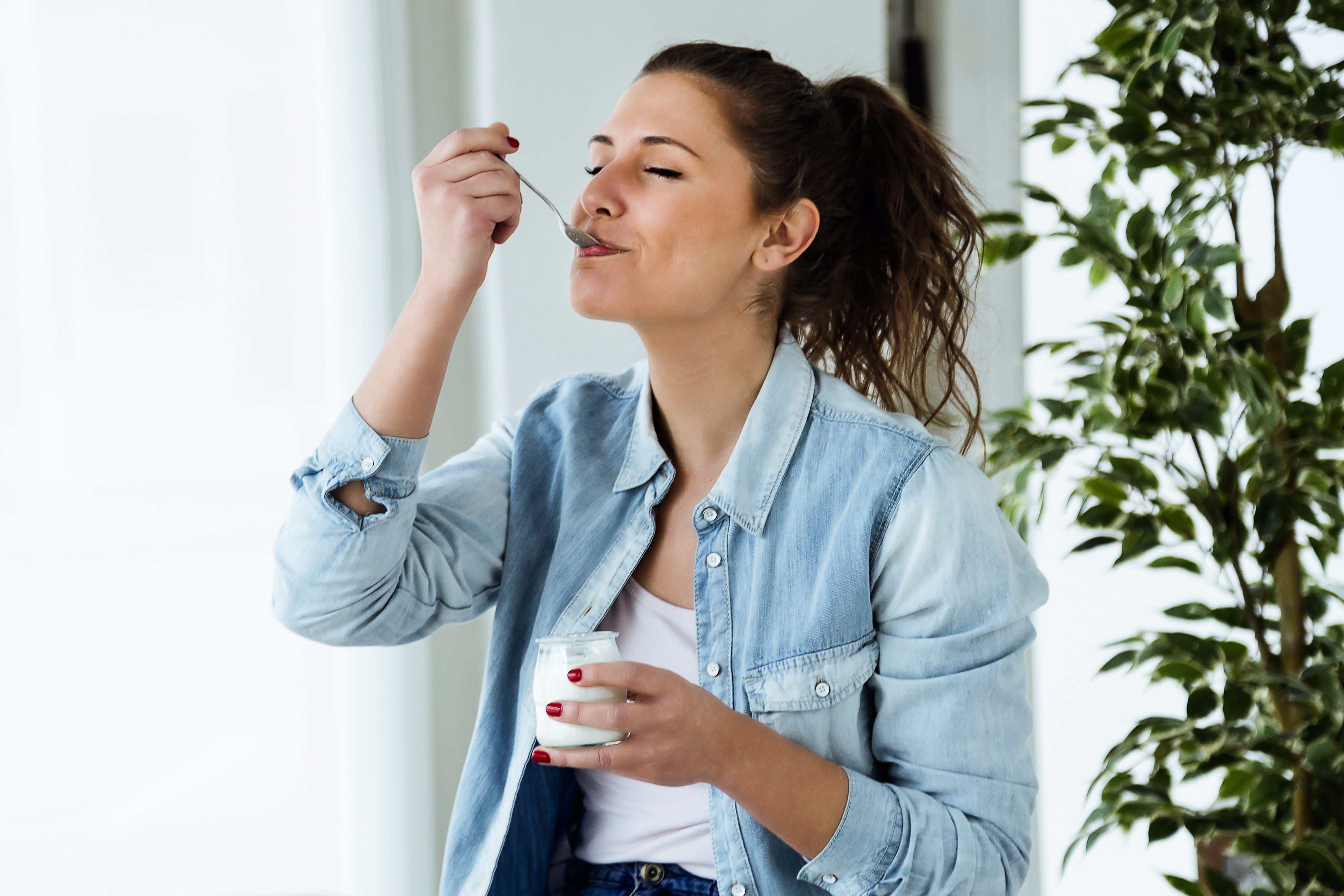 Portrait of beautiful young woman eating yogurt at home.