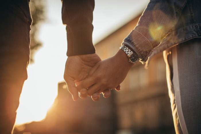 Couple sit on rock above sea, looking off|Couple sit on rock above sea, looking off|Couple holding hands