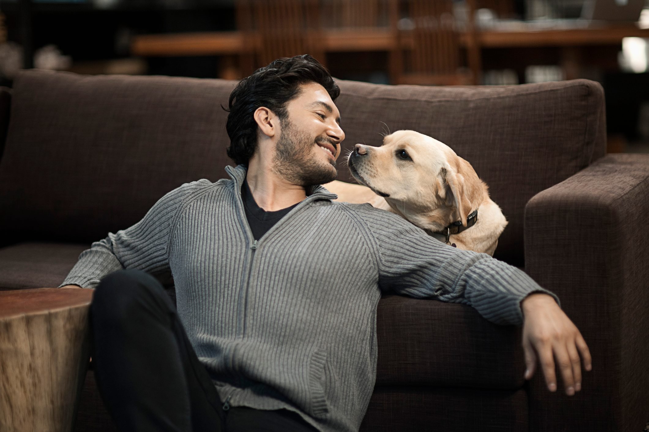 man sitting with dog in living room; their faces are very close to each others|