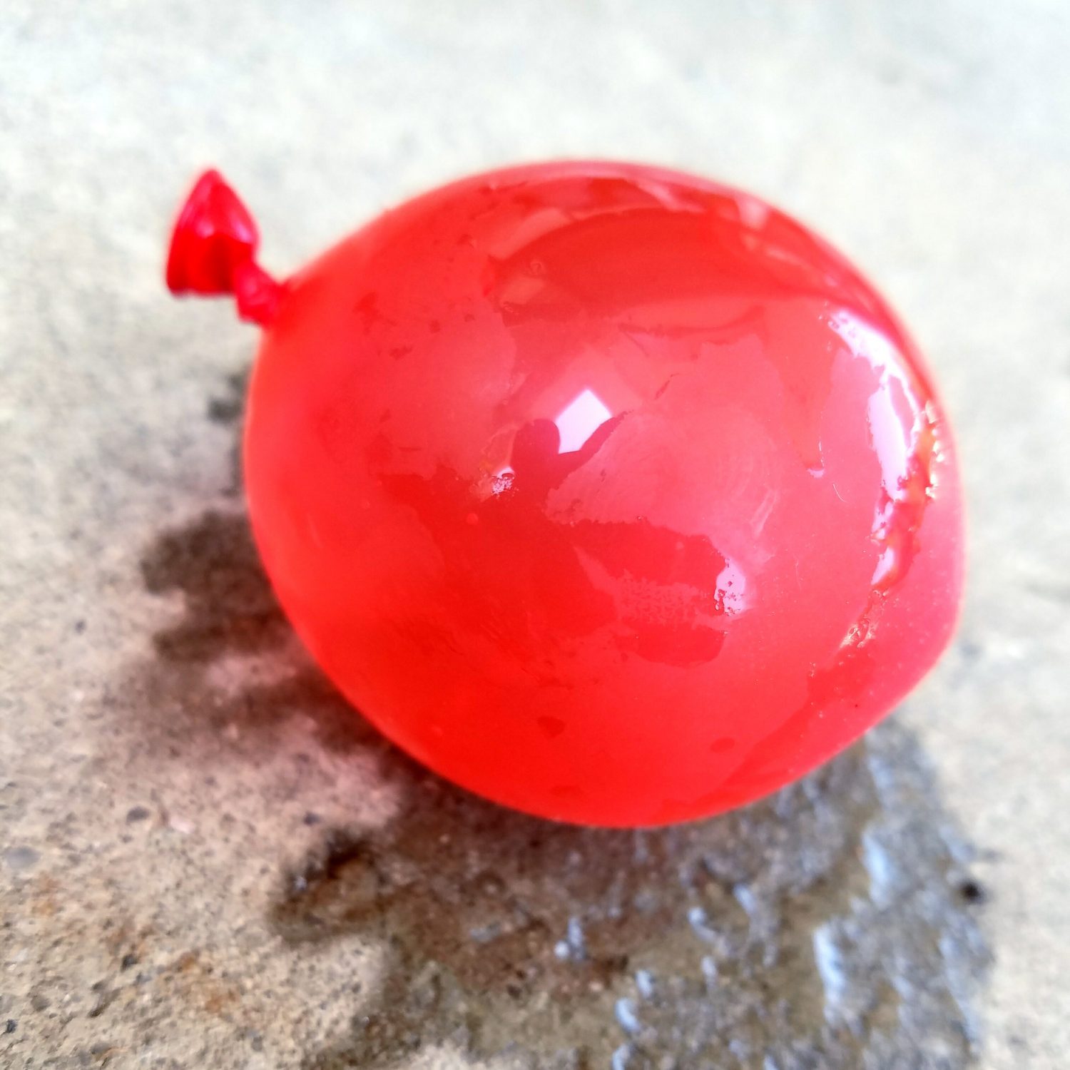 red Balloon Full Of Water with a water mark on the concrete under the balloon|