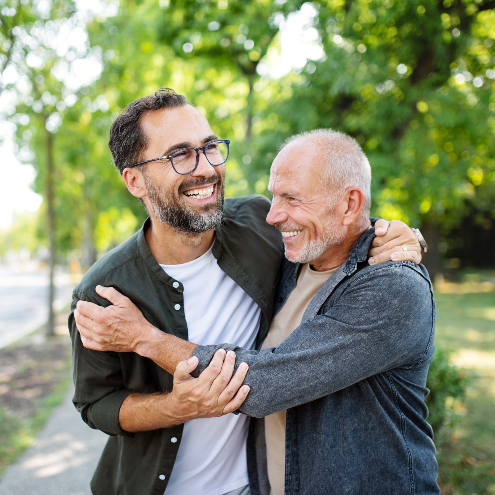 Senior man with his mature son embracing outdoors in park.|The Good Life book cover|portrait of Robert Waldinger on a grey studio background