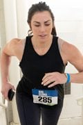 White woman in a ponytail and black tank top climbing stairs with a race bib.