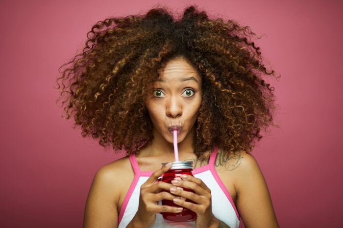 Delicious Colorful Plastic Drinking Straws|Beautiful young woman in summer clothes drinks from a straw against pink background