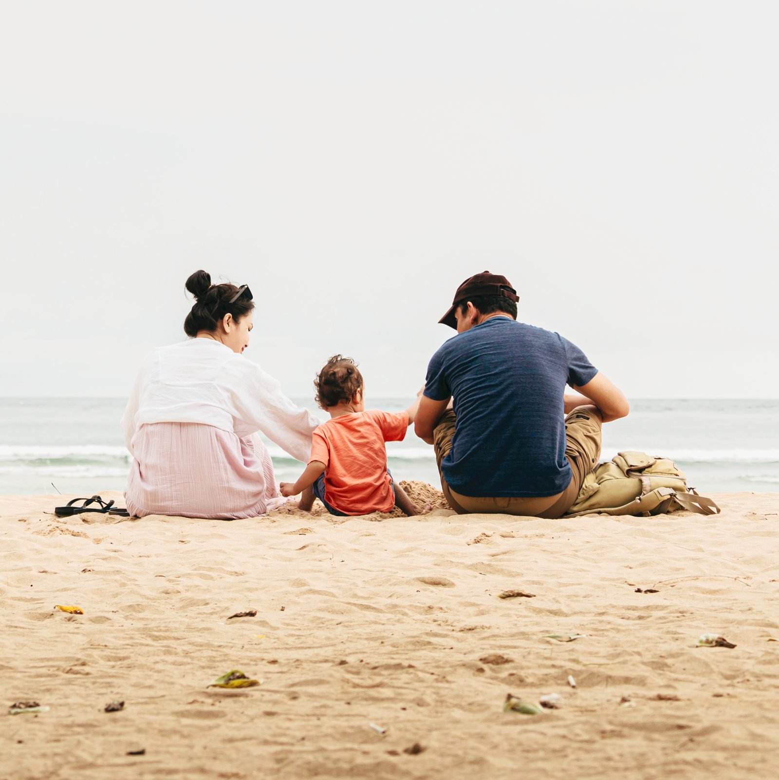 man, woman and child sit on beach together