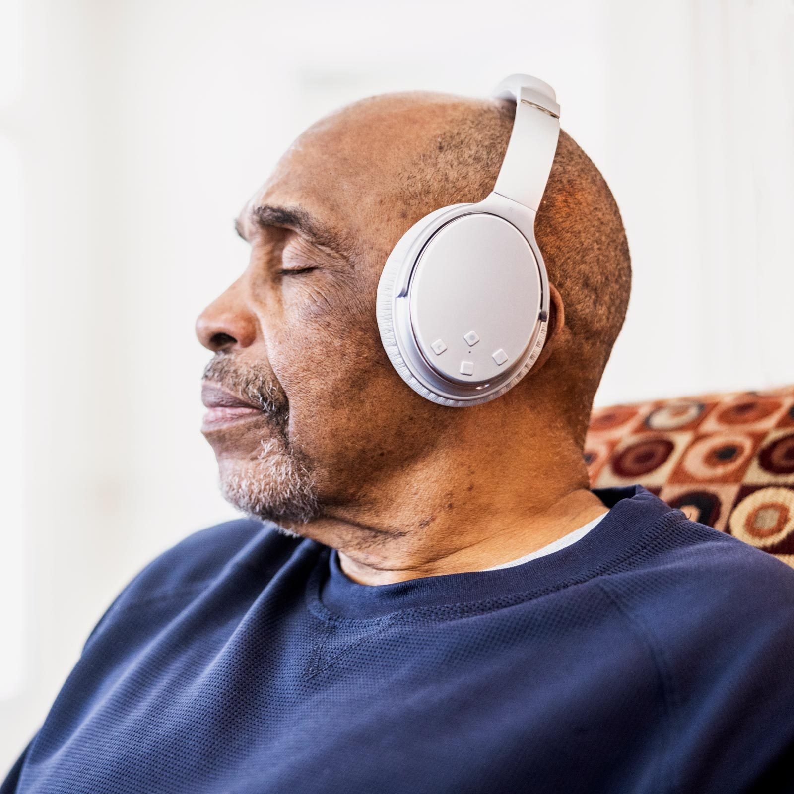 Senior man listening to music on wireless headphones at home|