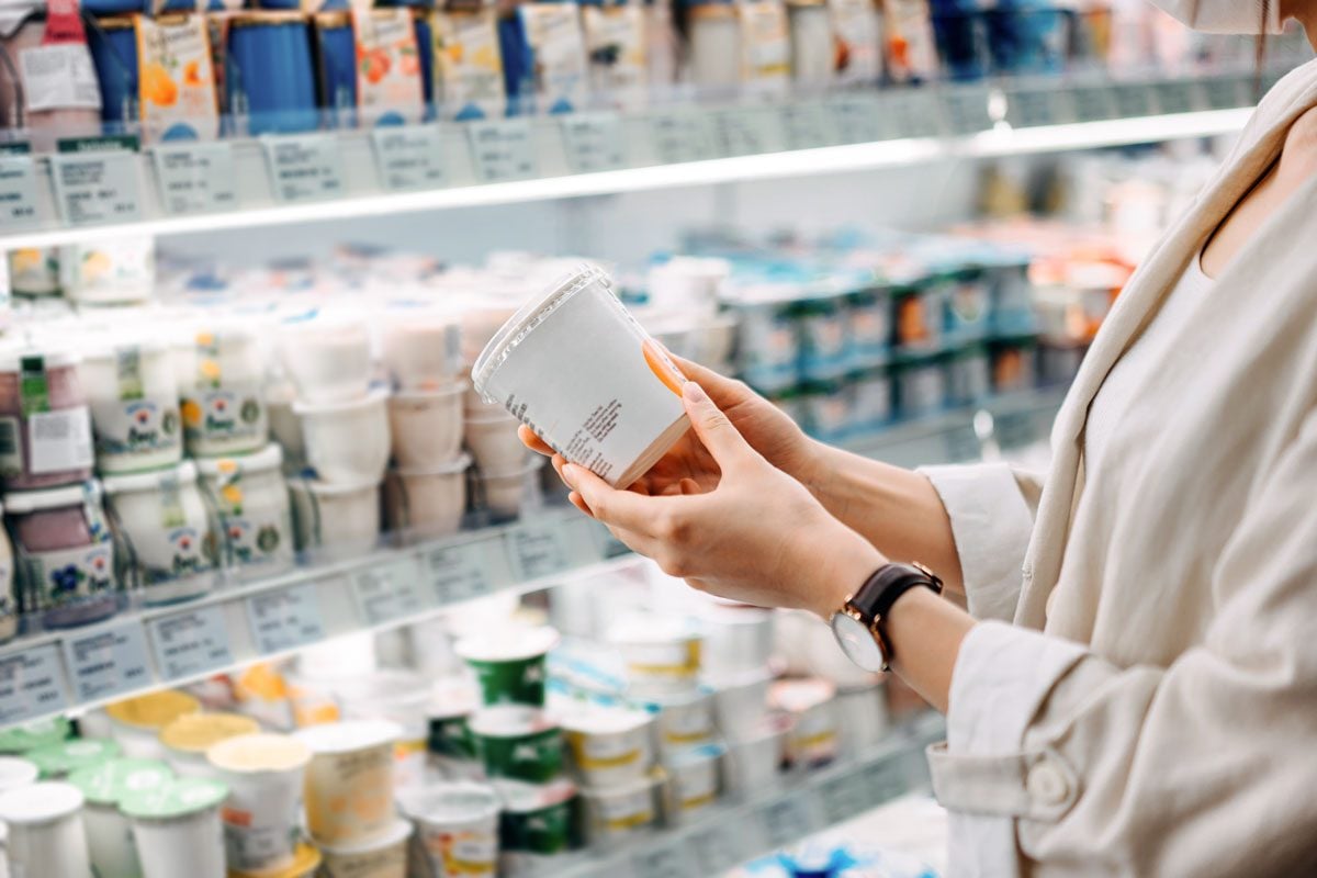 Cropped Shot Of an anonymous Woman Shopping In The Dairy Section Of A Supermarket. She Is Reading The Nutrition Label On A Container Of yogurt