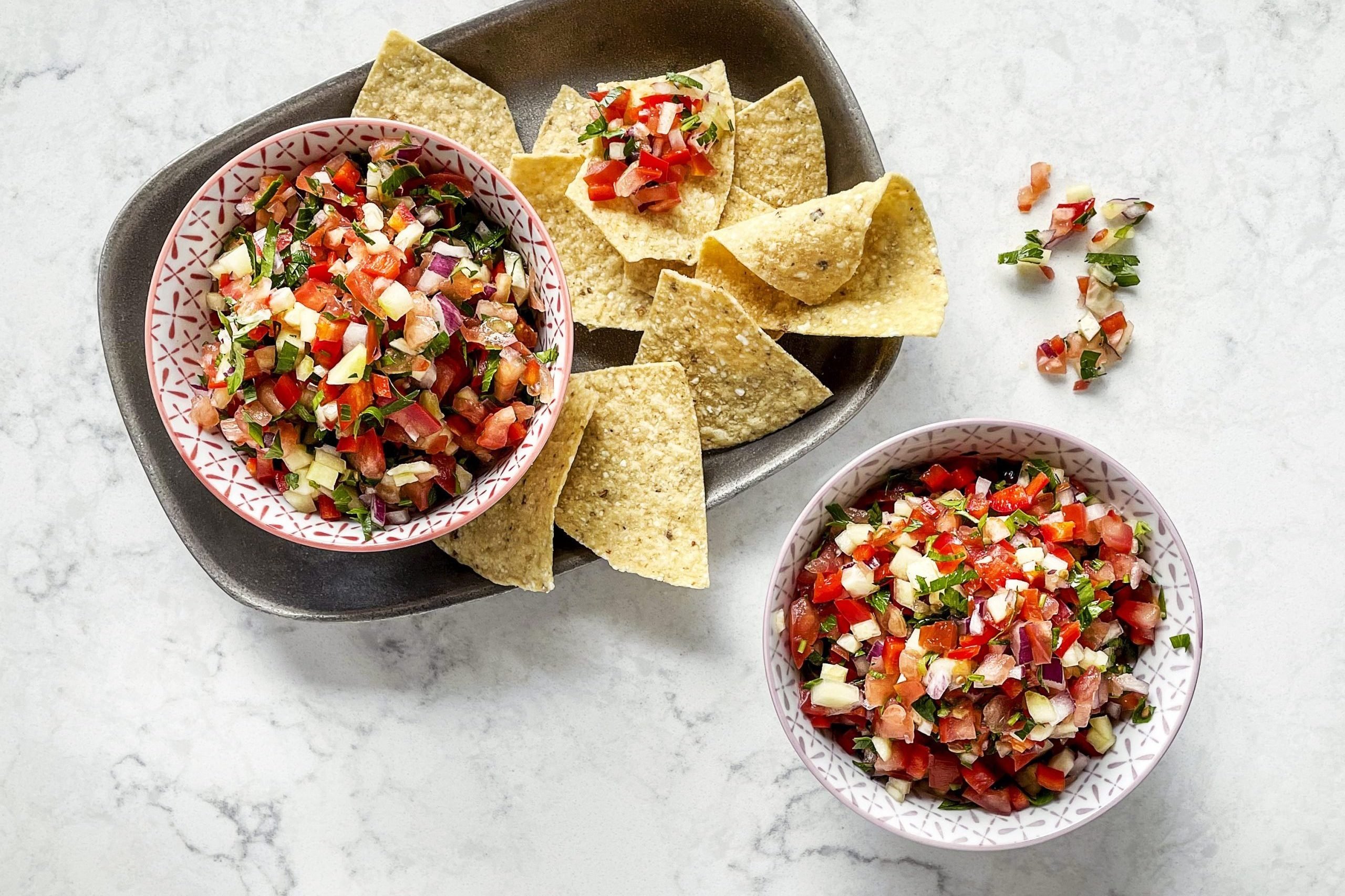 Bowls of salsa with corn chips on white, marble background