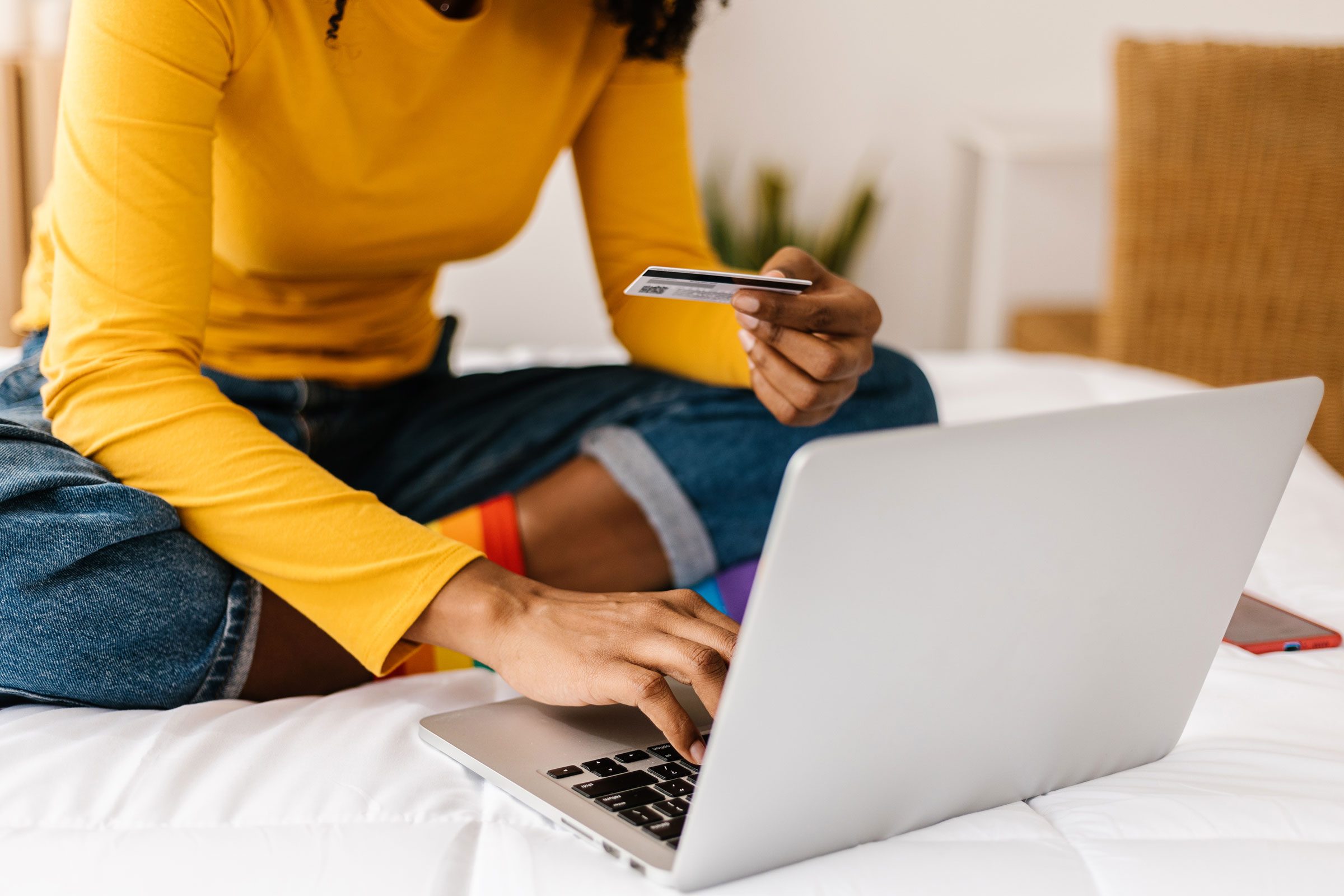 woman ordering home goods online with a credit card and laptop while sitting on a bed