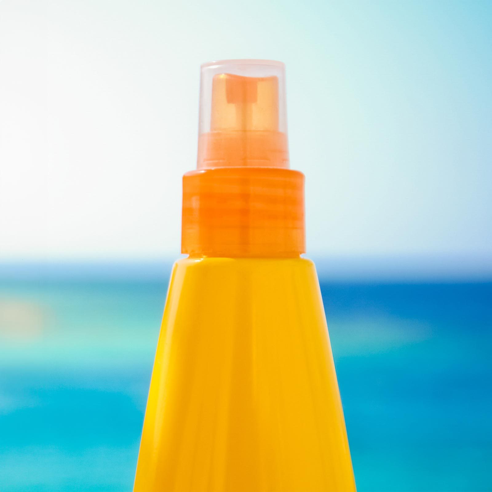 orange sunscreen bottle on a sunny day with blue sky and water in the background