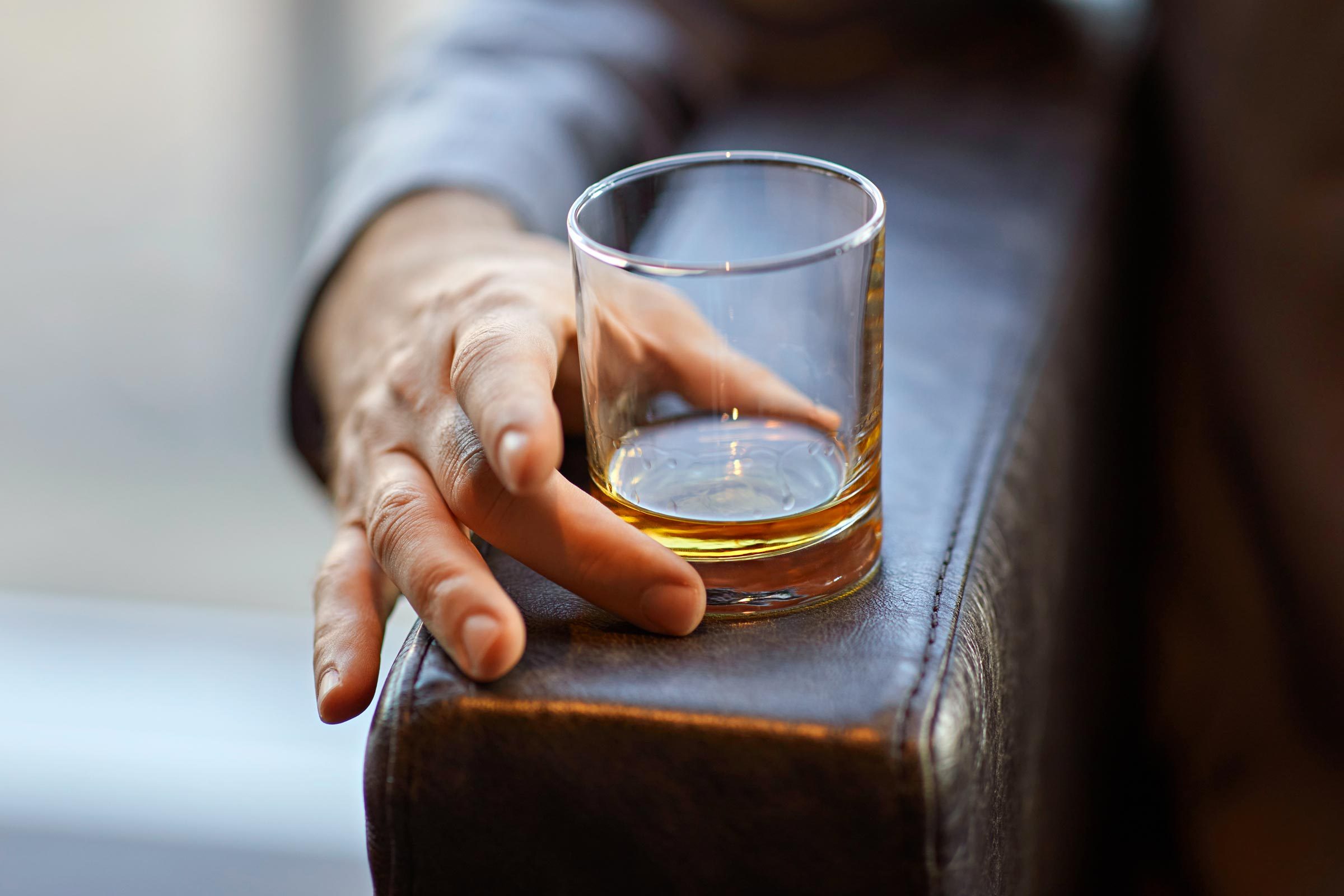 elderly hand with a glass of alcohol resting on a chair arm rest