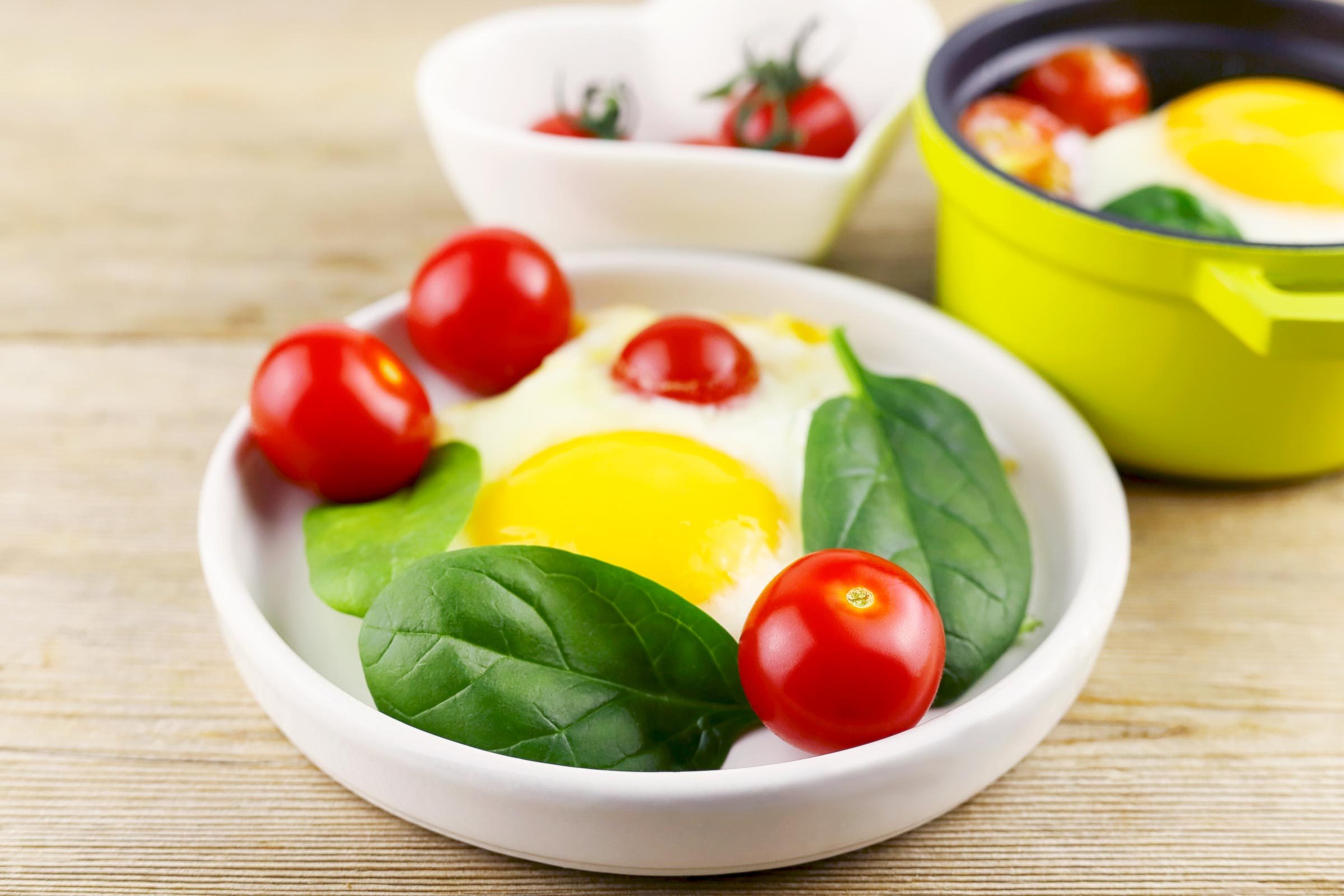 Fried eggs poached with tomatoes and spinach shakshuka on white plate