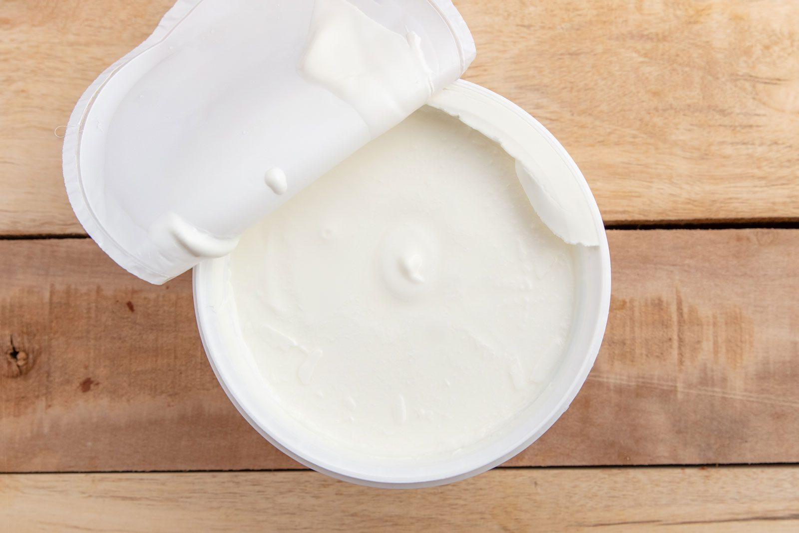 overhead view of an open container of yogurt on a wood surface