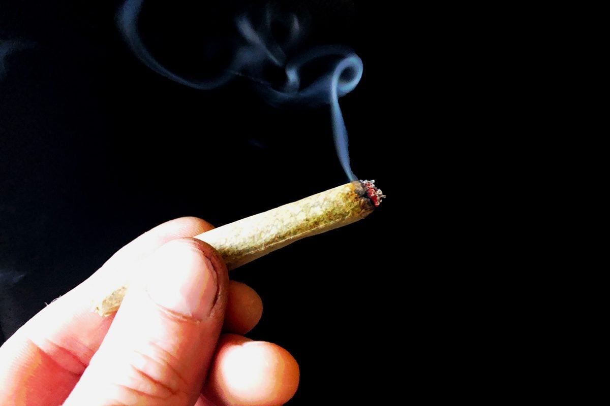 man's hand holding a lit joint against a black background