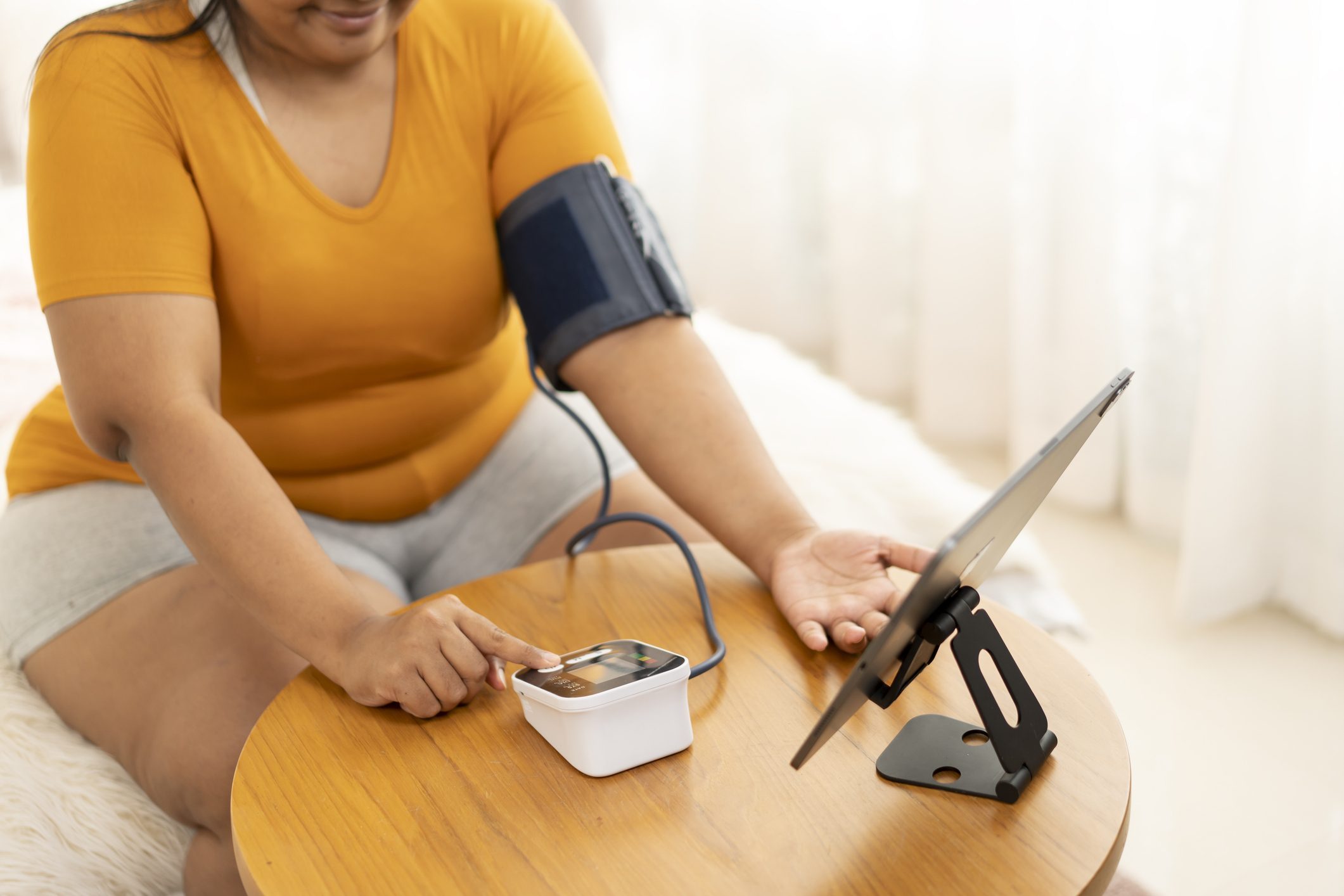 Plus size woman examining her blood pressure and having video call with doctor.