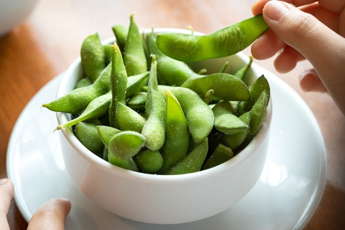 close up view of a hand grabbing some edamame from a bowl at a wood table in a restaurant