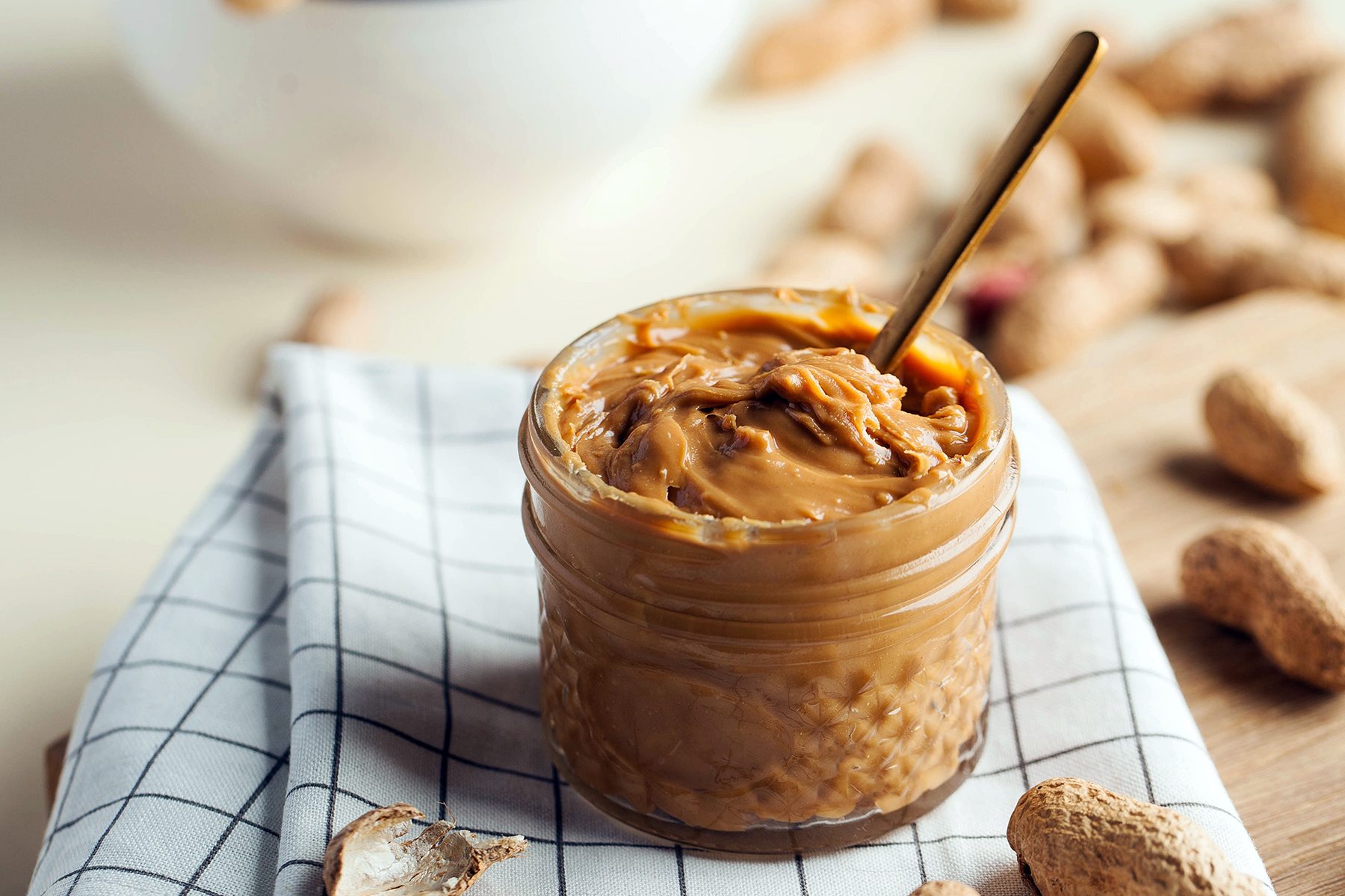 Closeup peanut butter in a glass jar, a handful of peanuts in shell. Foodphoto. Copy space. American culture. Breakfast, dessert for vegetarians.