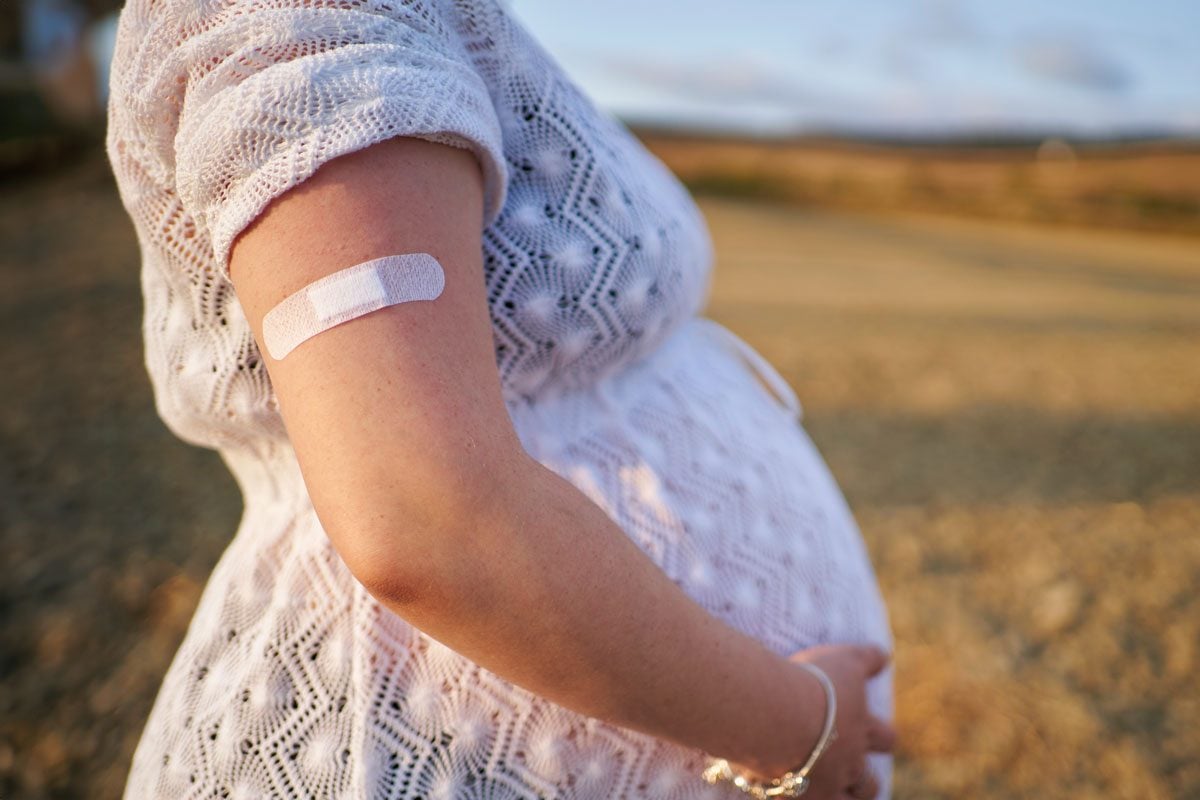 Side View of an anonymous pregnant woman outdoors on an autumn afternoon. On her arm is an adhesive bandage.|